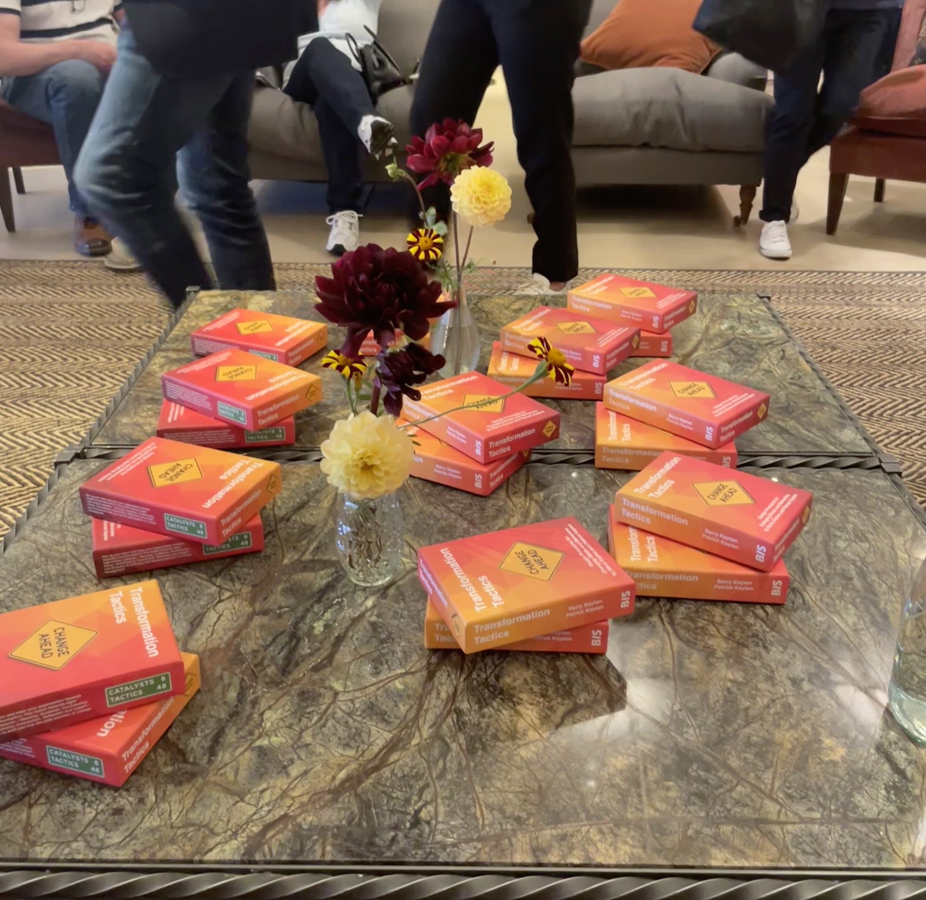 Orange boxes of Transformation Tactics cards on a marble coffee table. 